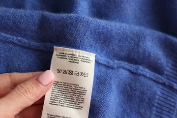 Woman holding clothing label in different languages on blue garment, closeup