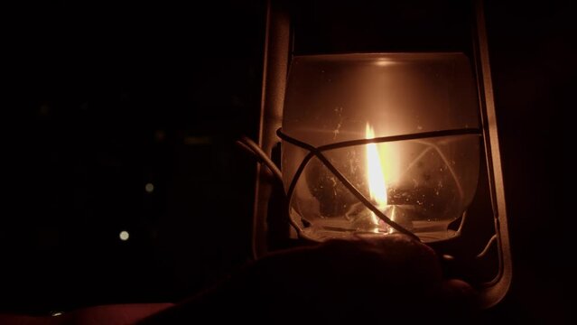 Dim night scene: Hand adjusts flame smaller in kerosene oil lantern
