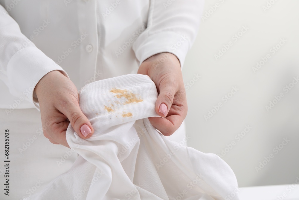 Poster Woman holding shirt with stain against light background, closeup