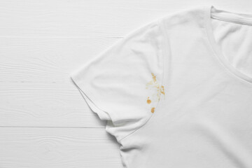 Stylish t-shirt with stain on white wooden table, top view. Space for text