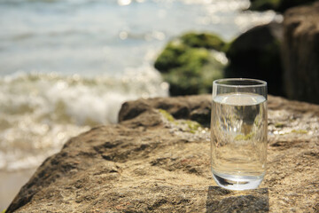 Glass of fresh water on stone near sea, space for text