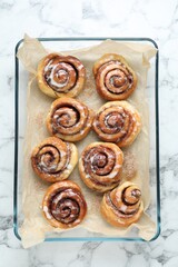Baking dish with tasty cinnamon rolls on white marble table, top view