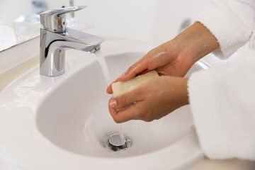 Washing hands of biracial woman in bathrobe in sunny bathroom