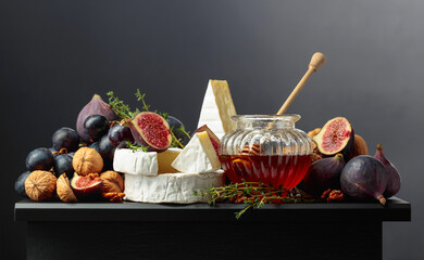 Camembert cheese with fruits and honey on a black background.