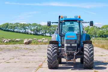 Blue tractor on a concrete pad with round bales of hay behind