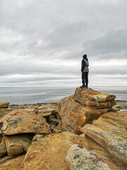 Obraz premium A girl on the shore of red stones next to the rocks of Two brothers on the Fishing Peninsula. The picturesque shore of the harsh Barents Sea. The North of Russia. The Kola Peninsula. The Arctic