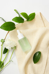 Close-up of the transparent serum bottle placed on a cloth towel with fresh green tea leaves and white flowers. Exquisite scene for vegan cosmetics advertisement.