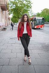 Beautiful Young Girl is Standing on the side Walk in Vilnius Old Town, Lithuania. Wearing Red jacket and Black Trousers. Beautiful Spring Day