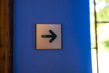 Black arrow sign hanging against blue wall of building for direction, pointing left. High quality photo. High quality photo