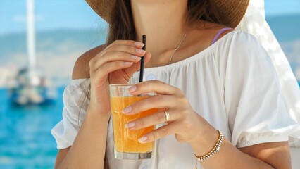 In a beach cafe gazebo on the pier, a brunette woman enjoys her orange juice with pure delight. Essence of summertime, holiday serenity, relaxation, and the call of travel