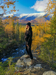 A girl on the background of an autumn Arctic landscape in the Khibiny mountains. Kirovsk, Kola Peninsula, Polar Russia. Autumn colorful forest in the Arctic, mountain hikes and adventures.