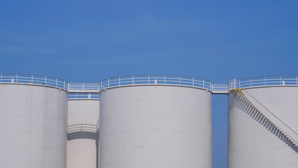 Row of white Storage Fuel Tanks in Oil Industrial area against blue sky background