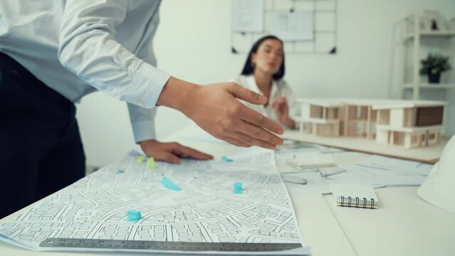 Skilled caucasian interior designer working with house model while discussing with asian architect engineer about house plan on meeting table with blueprint and house model scatter around. Immaculate.