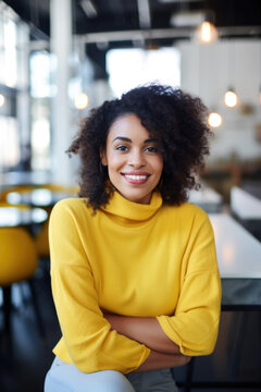 Portrait Of Beautiful Happy Black Woman In Yellow Sweater Looking At Camera In The Office, Blurred People In Background