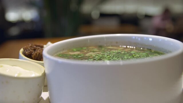 There is steam coming from the bowl of hot soup, croutons and sour cream next to it, the soup has just been prepared, the chef has just prepared mushroom soup with croutons and sour cream for lunch.