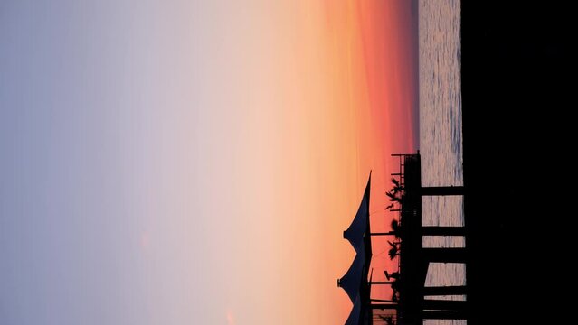 Tropical ocean beach with cafe on beach at dark sunset with purple orange sky. Vertical footage of water blue surface and dark coast. Travel, tourism, journey, destination on resort for relax concept.