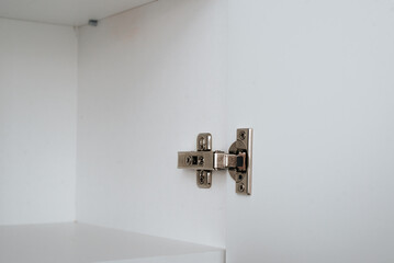 Close-up of a steel hinge on a wooden open drawer door, fittings