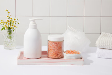 Unbranded pump bottle placed on a tray with a jar and a bowl of pink himalayan salt. A stack of towels displayed. Empty label for cosmetic product or shampoo advertising