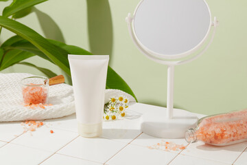 Blank label tube in white color displayed with a rounded mirror and white towel. Natural pink himalayan salt inside glass bowl and bottle. Skin care product concept