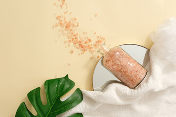View from above of a bottle of pink himalayan salt placed on a mirror in round shaped. Green leaf...