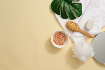 A ceramic bowl containing pink himalayan salt decorated with some body care products. A green leaf decorated. Beige background with copy space. Pink Himalayan salt is used in some bath salts