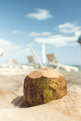 green Coconut in the sand with a straw in it