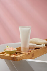 A dish of pink himalayan salt decorated with empty label tube, foot scrubber brush and a stack of towels. Bathroom view. Container packaging of skin care branding