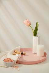 A pot with tulip flower displayed on tray with a candle and palo santo wood smoke. Ceramic bowl of pink himalayan salt on white towel. Blank space for beauty products promotion