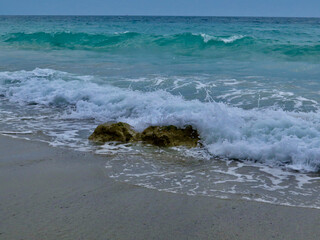 Fototapeta na wymiar Waves crash on rocks on the beach. Small waves roll onto the stones lying on the sandy beach.
