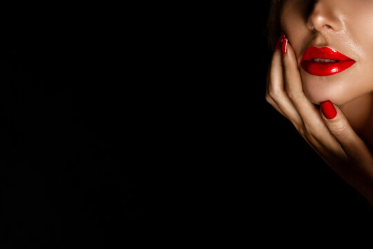 Beautiful woman in elegant makeup with red lips and nails posing sensually on a black background.