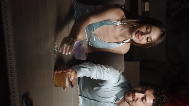 A couple in love drinks cocktails and takes a photo on the terrace in a hotel at sunset. Vacation concept. Vertical video