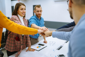 Obraz premium A group of people in an office meeting collectively resolve an issue by raising their hands. Colleagues in the office sign an agreement, hands forward. Concept of business, negotiations.