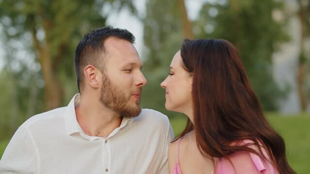 Mid shot young couple biting grape on picnic and kisses. Cute wife kiss husband after feeds him a sweet grape in nature. Beautiful family couple having romantic date lunch outdoors