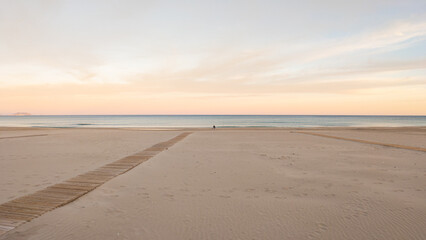 Big sea beach at sunset and the horizon. Empty sea beach with yellow sand. Pink sunset over the sea. The coast in the evening at the resort. Alicante, Costa Blanca, Spain