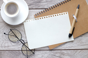 on a closed notebook there is a blank torn page near a cup of coffee and glasses