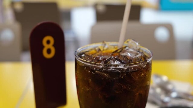 A glass filled with ice and cola and a straw sticking out on a table then a queue number, Food and Beverage.