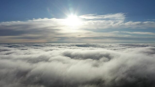 Slow aerial flight toward bright, behind cloud sun above heaven like cloud top