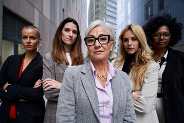 Empowered group of multiracial businesswomen looking at camera with confidence, standing outdoors corporative district. - obrazy, fototapety, plakaty