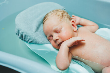 A newborn baby lies on a stand in a bathtub for bathing. Bathing the baby. Hygiene of newborns and...