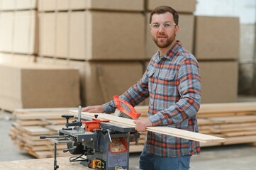 A carpenter works on woodworking the machine tool. Man collects furniture boxes. Saws furniture details with a circular saw. Process of sawing parts in parts. Against the background of the workshop.