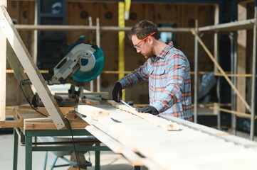 A carpenter works on woodworking the machine tool. Man collects furniture boxes. Saws furniture details with a circular saw. Process of sawing parts in parts. Against the background of the workshop.