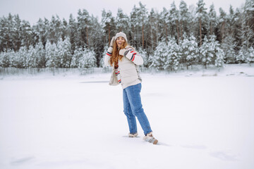 Fototapeta na wymiar Beautiful young woman in winter clothes enjoying the winter forest. Behind her is a snow-covered lake. Happy winter time. Christmas.