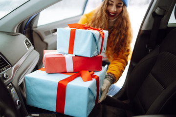 Happy young woman putting New Year's gifts into a car. A wonderful atmosphere of celebration and...