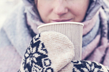 Young woman warmly dressed drinking hot mulled wine having knitted gloves on hands