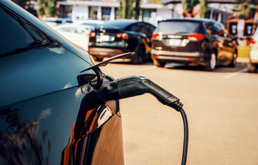 Charging modern electric vehicle in a parking lot with charging electric cable plugged in, close up...