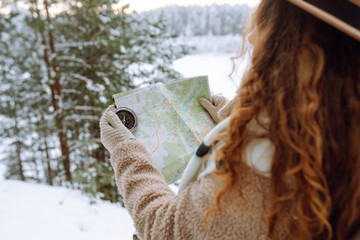Beautiful woman traveler holds a compass and map in her hands. She is wearing a winter jacket, hat, scarf and backpack. Enjoying winter travel. Active lifestyle. Travel concept.