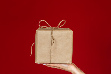 close-up of a woman's hand holding a gift wrapped in kraft paper. isolated on a red background. Mock up. Copy space. Eco gift packaging. Handmade Packaging 