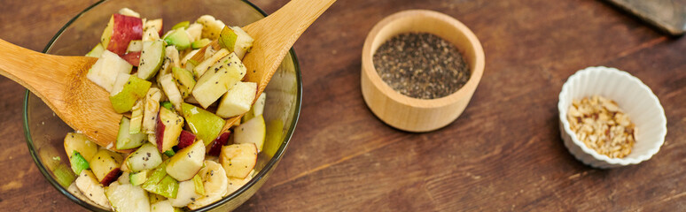 glass bowl with vegetarian fruit salad and wooden spatulas near sesame seeds and nuts, banner