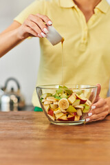 cropped view of woman pouring honey on fresh fruit salad in glass bowl, delicious plant-based diet