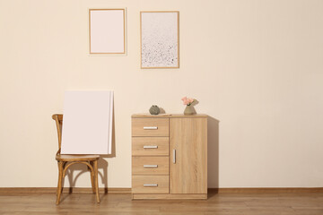 Wooden cabinet, decor and posters in room with beige wall